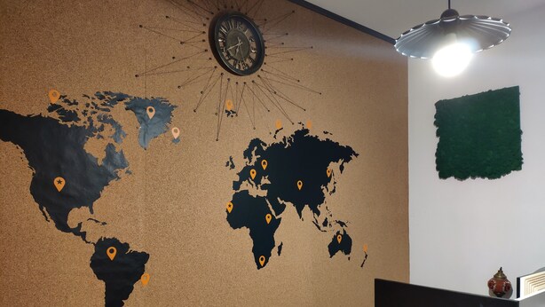 Un mapa del mundo con marcadores de ubicación en un panel de corcho, un reloj y una lámpara colgante.