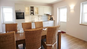 Une cuisine moderne avec des meubles blancs, un four encastré et un coin repas comprenant des chaises en osier et une table en bois.