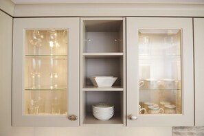 A kitchen cabinet with three glass-fronted shelves, each containing kitchenware.