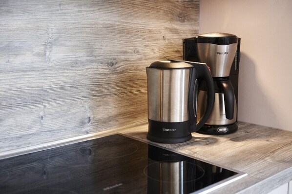 A modern kitchen with a wooden backsplash, a black induction cooktop, and two coffee makers, one branded 'PHILIPS' and the other 'BAMTEC'.