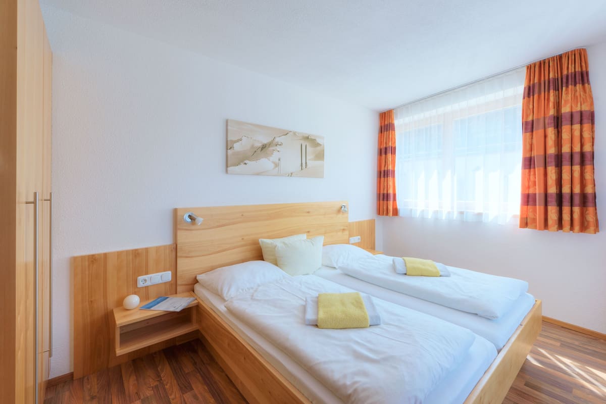 Uma cama de casal com roupa de cama branca, uma cabeceira de madeira e uma mesa de cabeceira com abajur e um livro.
