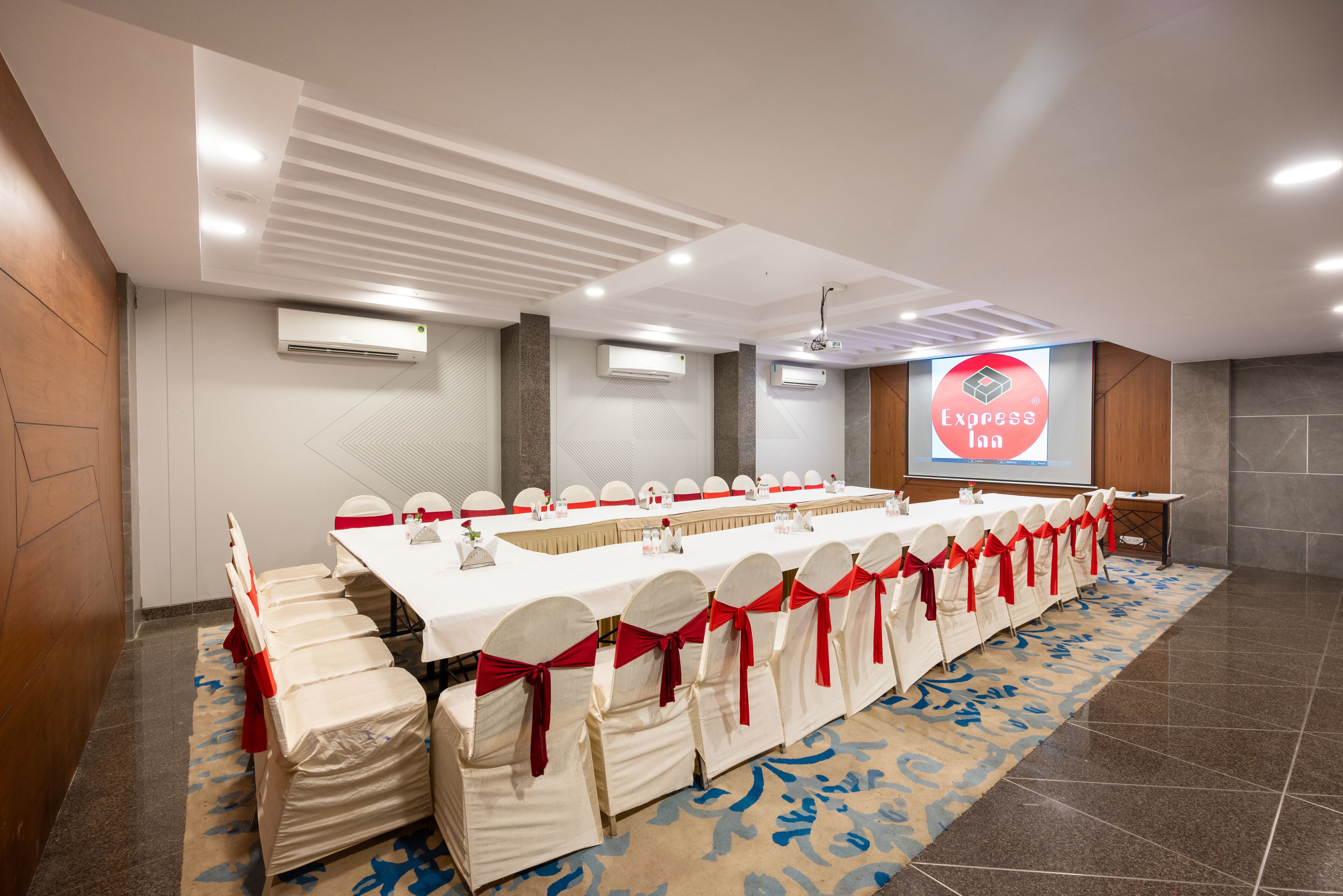 A conference room with a long table, chairs with red sashes, and an air conditioning unit on the wall.