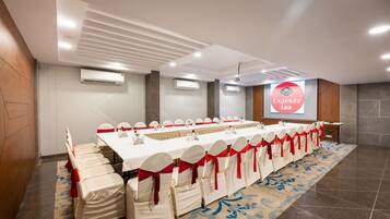 A conference room with a long table, chairs with red sashes, and an air conditioning unit on the wall.