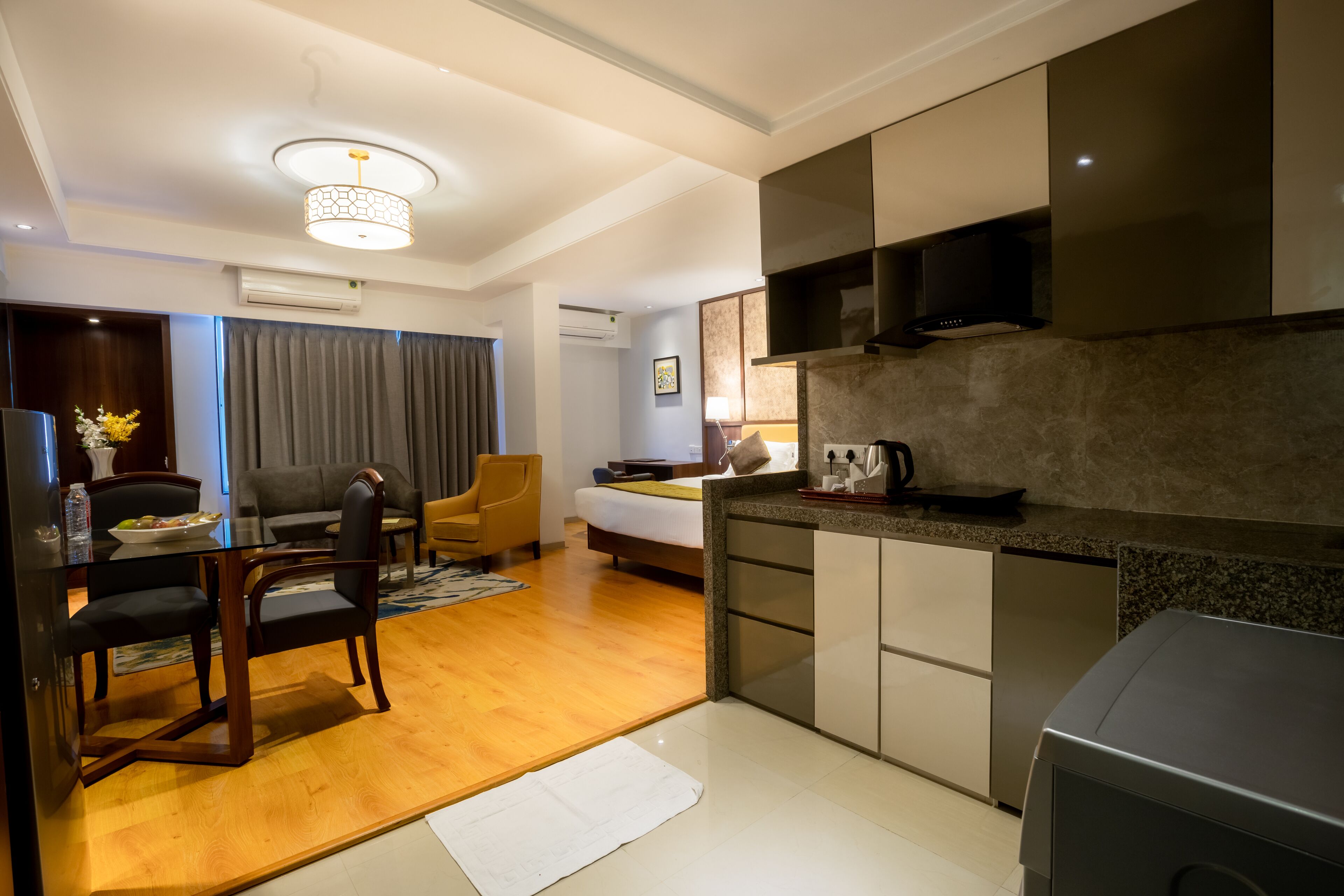 A modern hotel room with a dining area, a bed, a kitchen with a microwave, and a large window.
