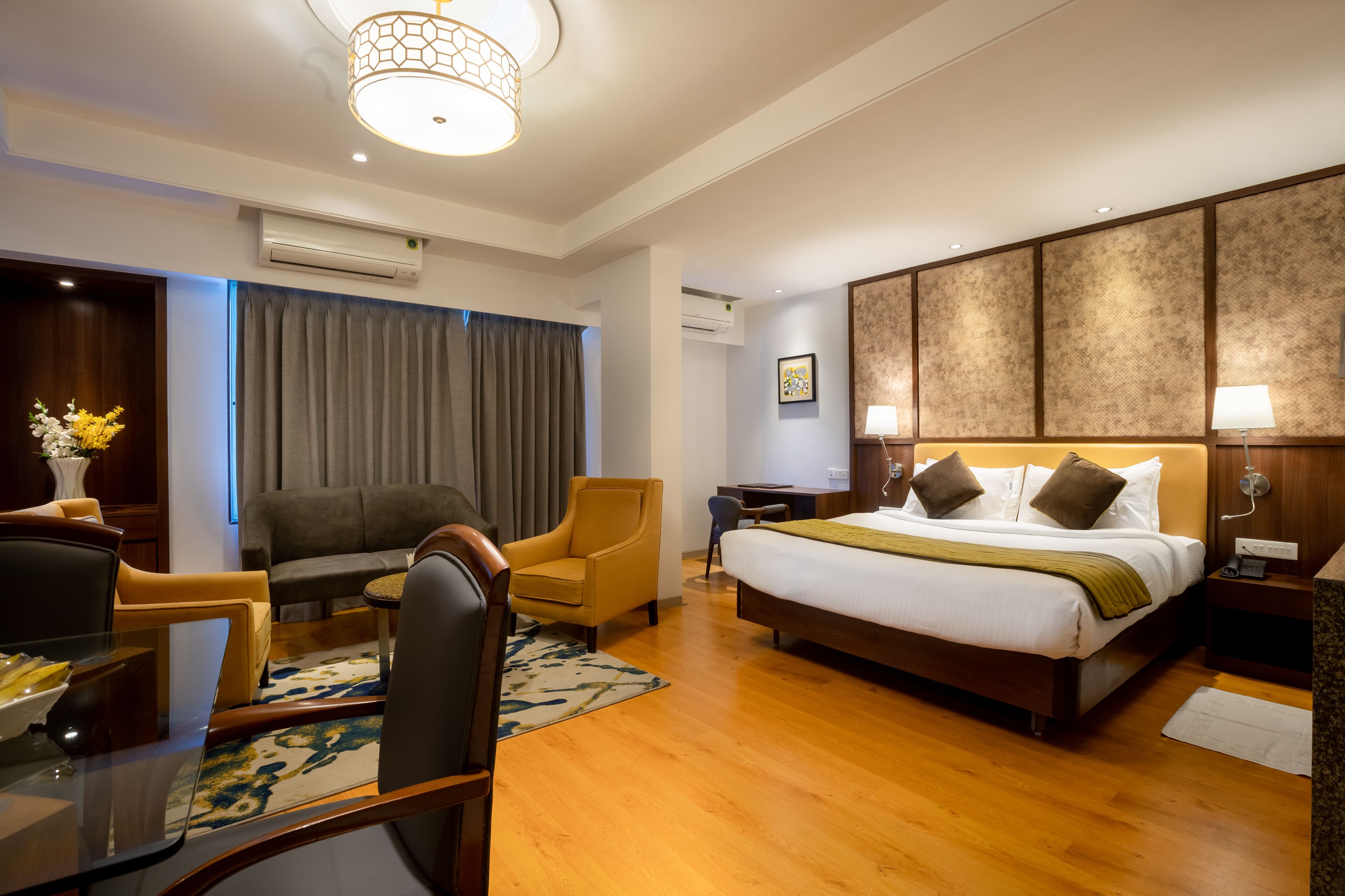 A hotel room with a large bed, a desk, a chair, a sofa, and a lamp.