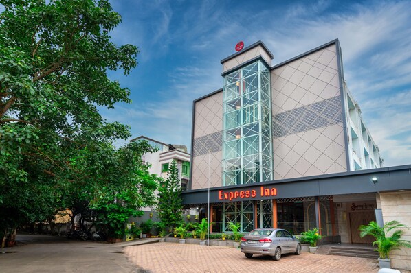 Un hotel llamado 'Express Inn' con un diseño arquitectónico moderno, destacando una fachada de vidrio y un área de entrada bien cuidada con plantas en macetas.
