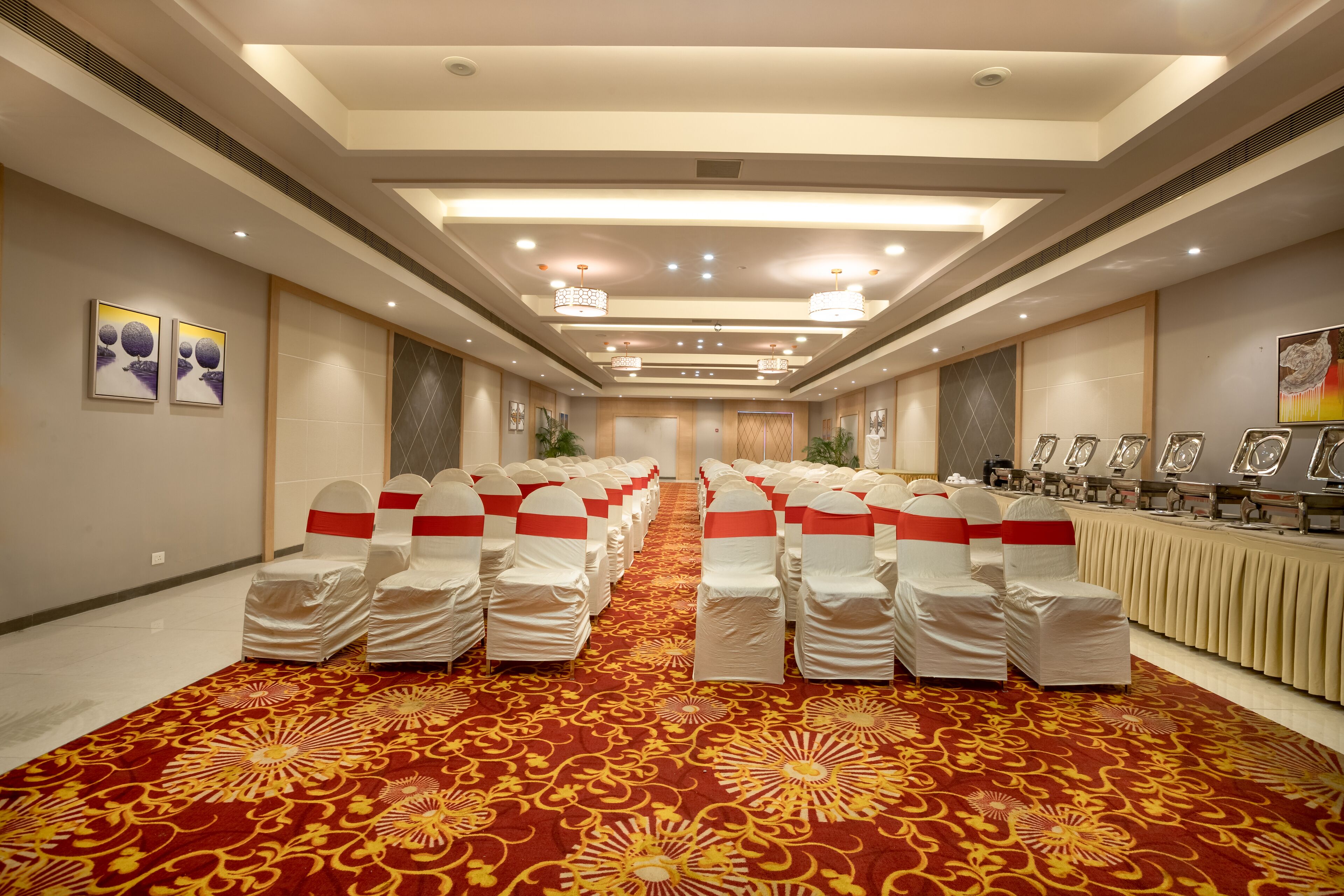Un salón de conferencias con filas de sillas, una alfombra estampada e iluminación en el techo.