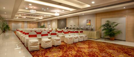 A banquet hall with rows of white chairs with red sashes, a red patterned carpet, and a ceiling with recessed lighting.