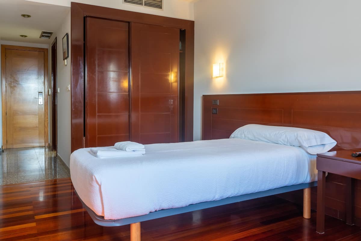 Quarto de hotel com cama de madeira, mesa de cabeceira, guarda-roupa e luminária na parede.