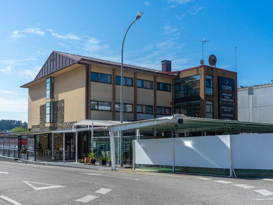 Un edificio moderno con una zona de entrada cubierta, ventanas amplias y un cartel publicitando papas fritas.