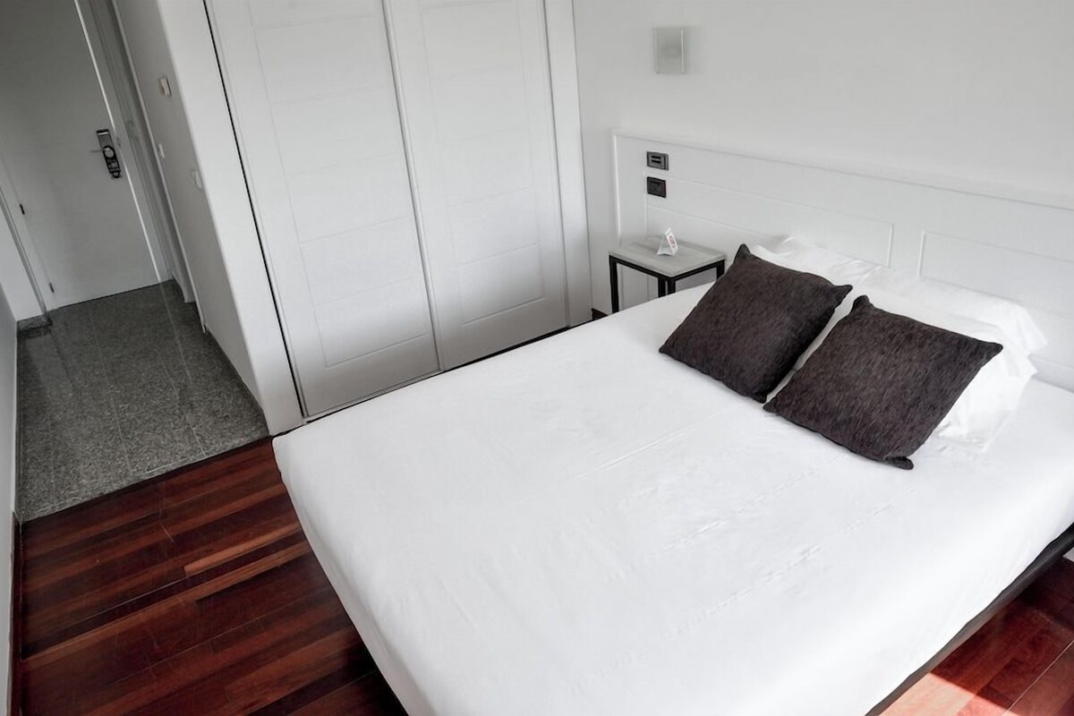 A hotel room with a large bed, a bedside table, and a wardrobe.
