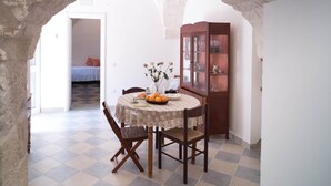 Uma área de refeições com uma mesa posta para dois, um armário de madeira com portas de vidro e um chão quadriculado.