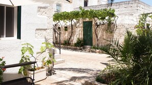 Um pátio com um edifício branco, uma porta verde e uma pérgola coberta de trepadeiras.