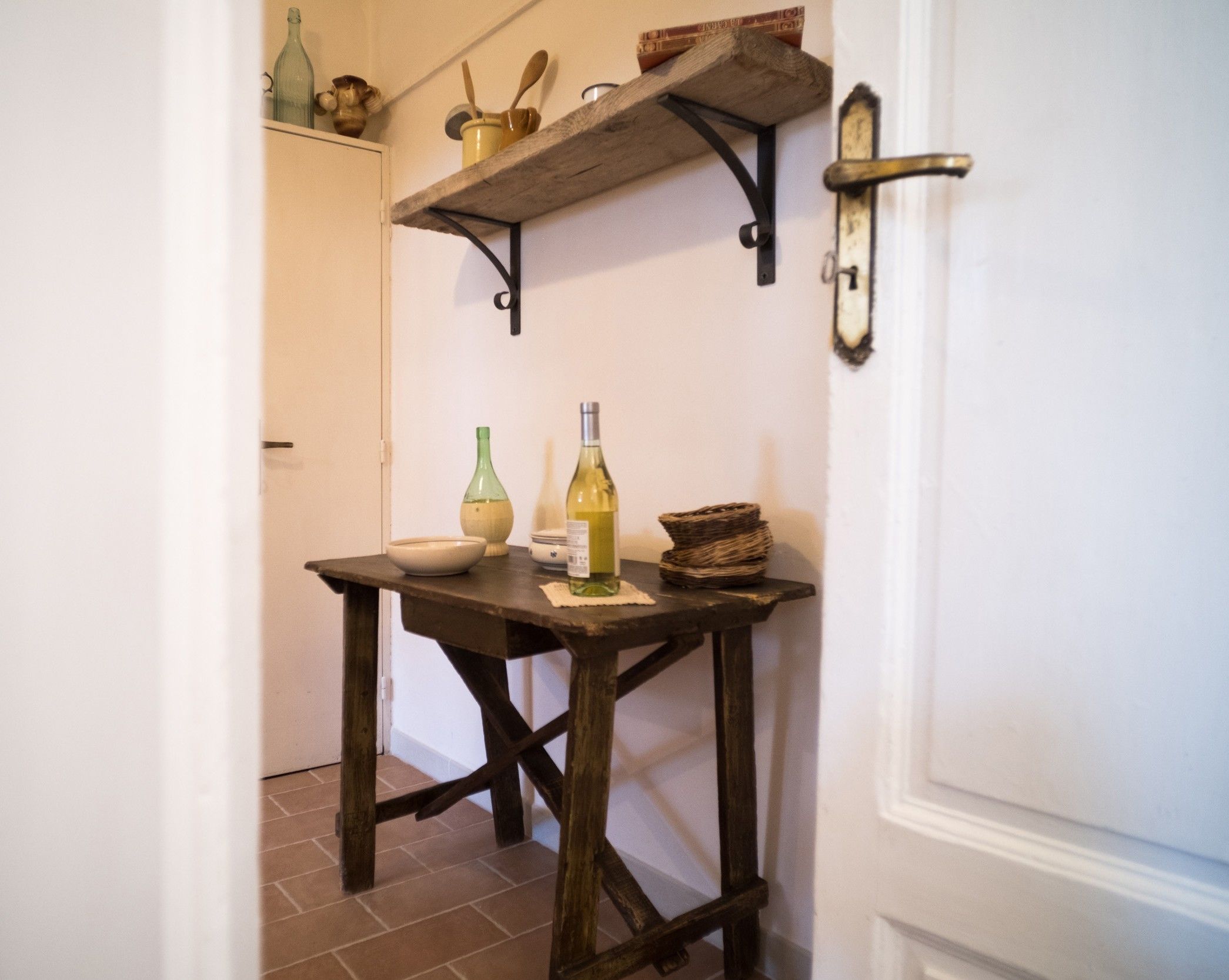 A kitchen with a wooden table, a white door, and a shelf above it.