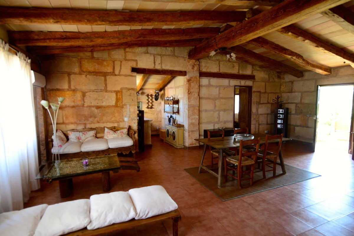 Un interior rústico con paredes de piedra, vigas de madera, un sofá, una mesa de comedor y un banco.