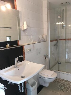 A modern bathroom with a white sink, toilet, and glass-enclosed shower. - Landhotel Steffen (Lieser)