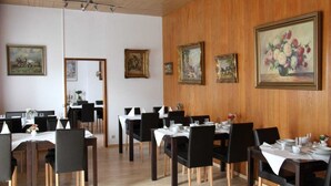 A restaurant with wooden paneling, black chairs, white tablecloths, and framed paintings on the walls. - Hotel Humboldt (Bad Kissingen)