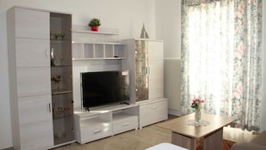 A modern living room with a flat-screen TV, built-in shelving, and a dining area with a table and chairs. - Hotel Humboldt (Bad Kissingen)