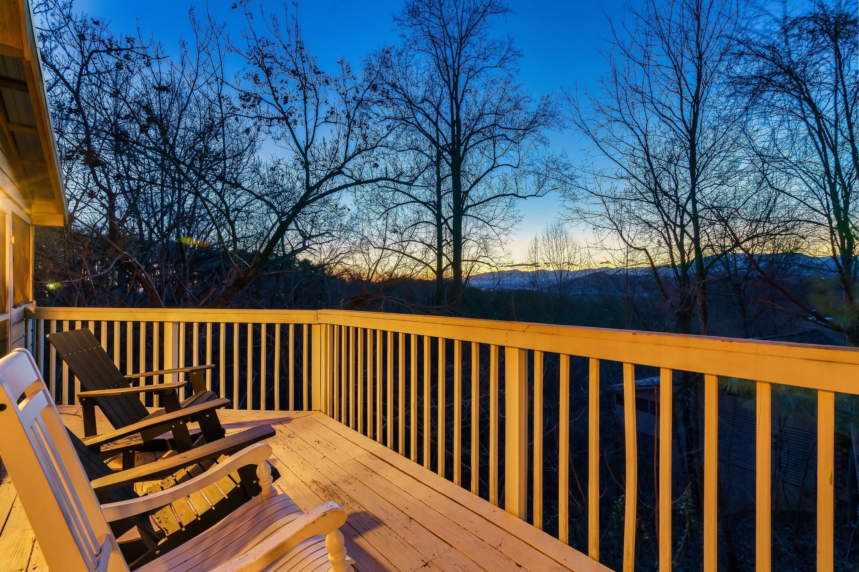 A wooden deck with two Adirondack chairs and a bench, overlooking a mountainous landscape.