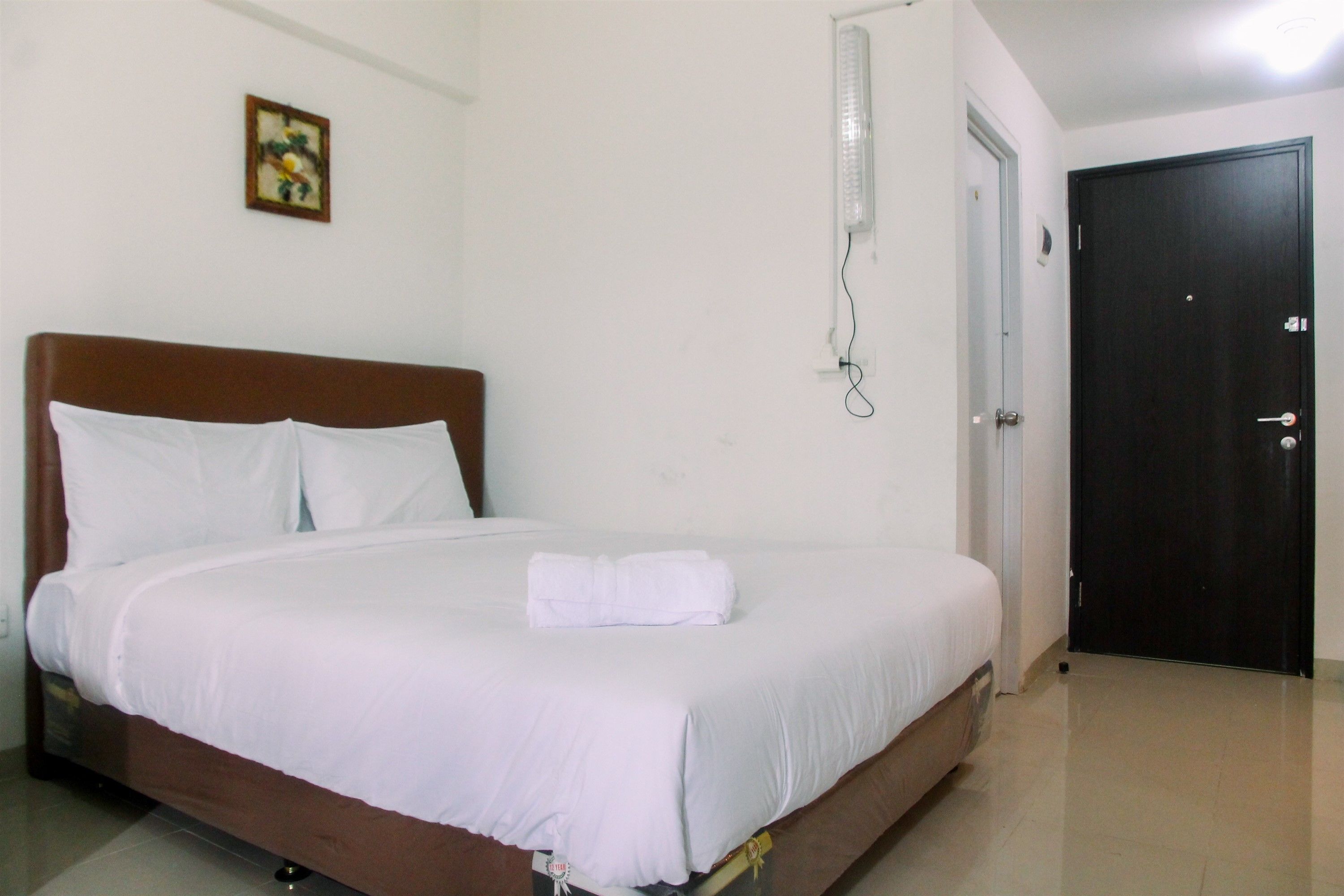 A neatly made bed with white linens, a brown headboard, and a single white towel on the bed.