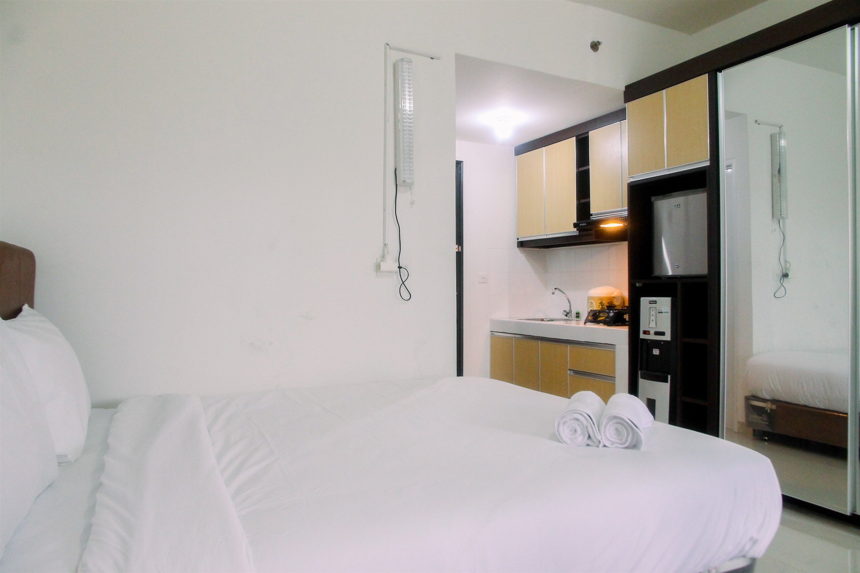 A hotel room with a bed, a bathroom, a kitchenette, and a mirror.