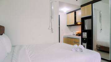 A hotel room with a bed, a bathroom, a kitchenette, and a mirror.