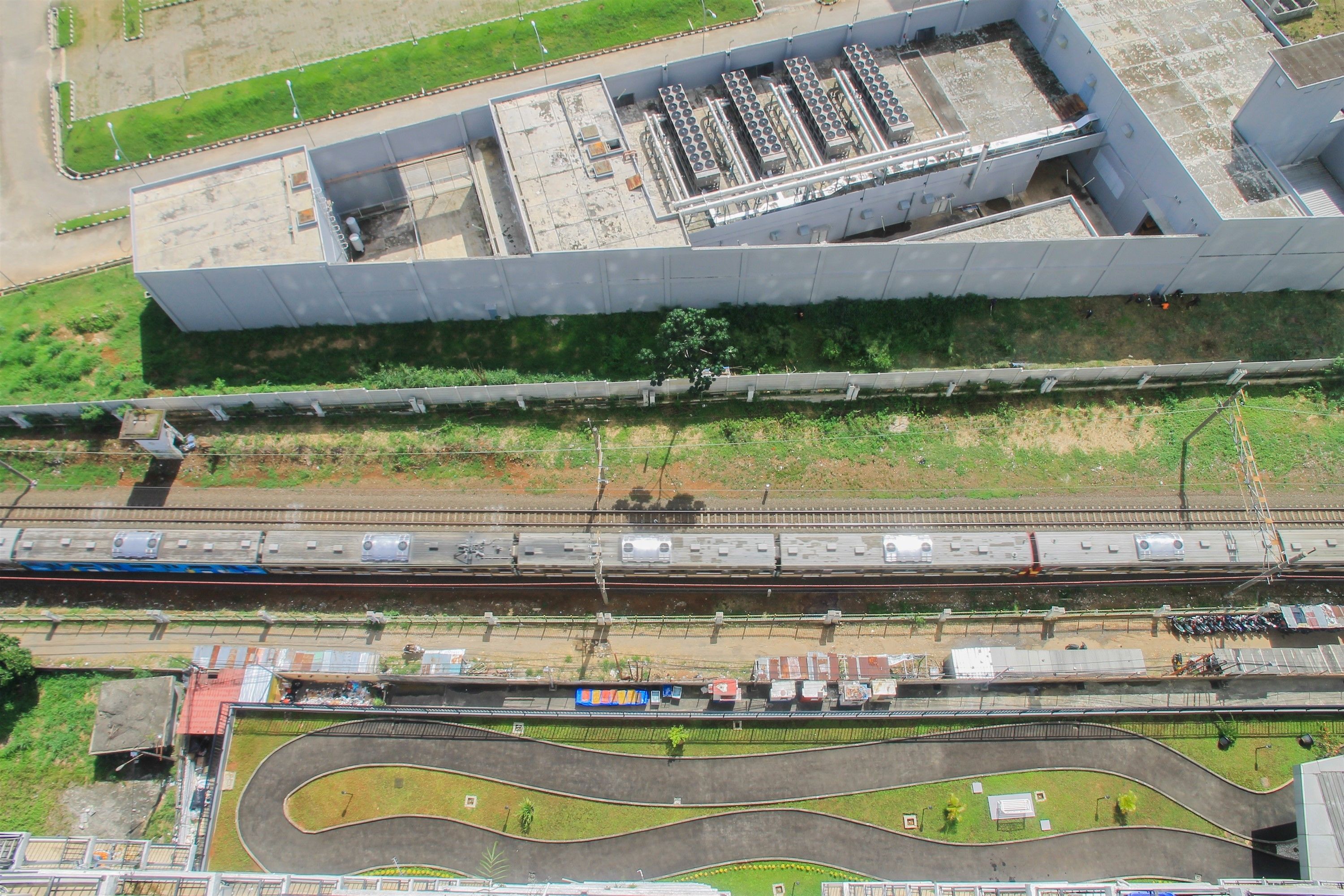 An aerial view of a modern building with a flat roof and large windows, adjacent to a railway track with multiple trains.