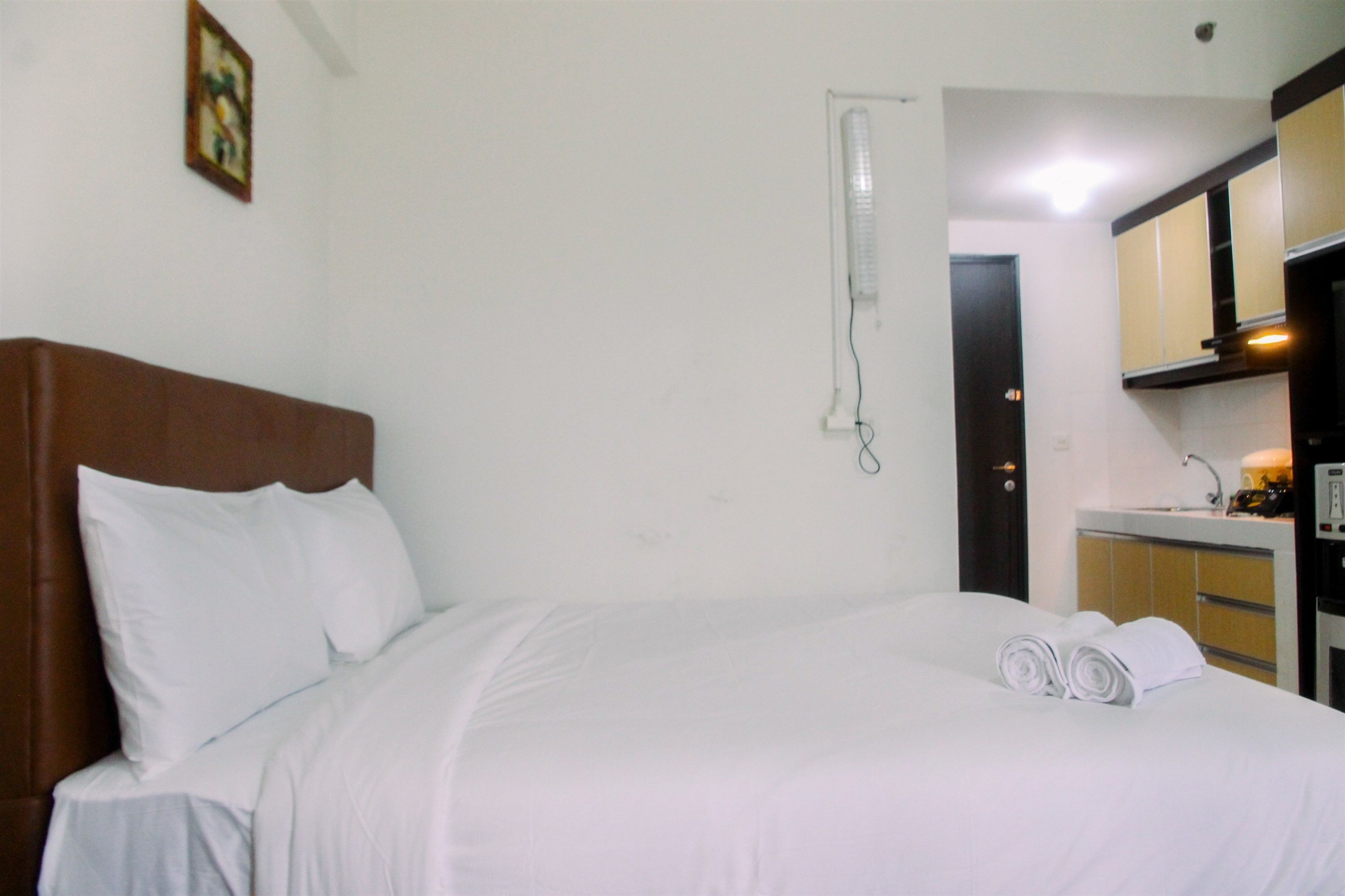 A hotel room with a bed, a small kitchenette, and a door leading to another room.