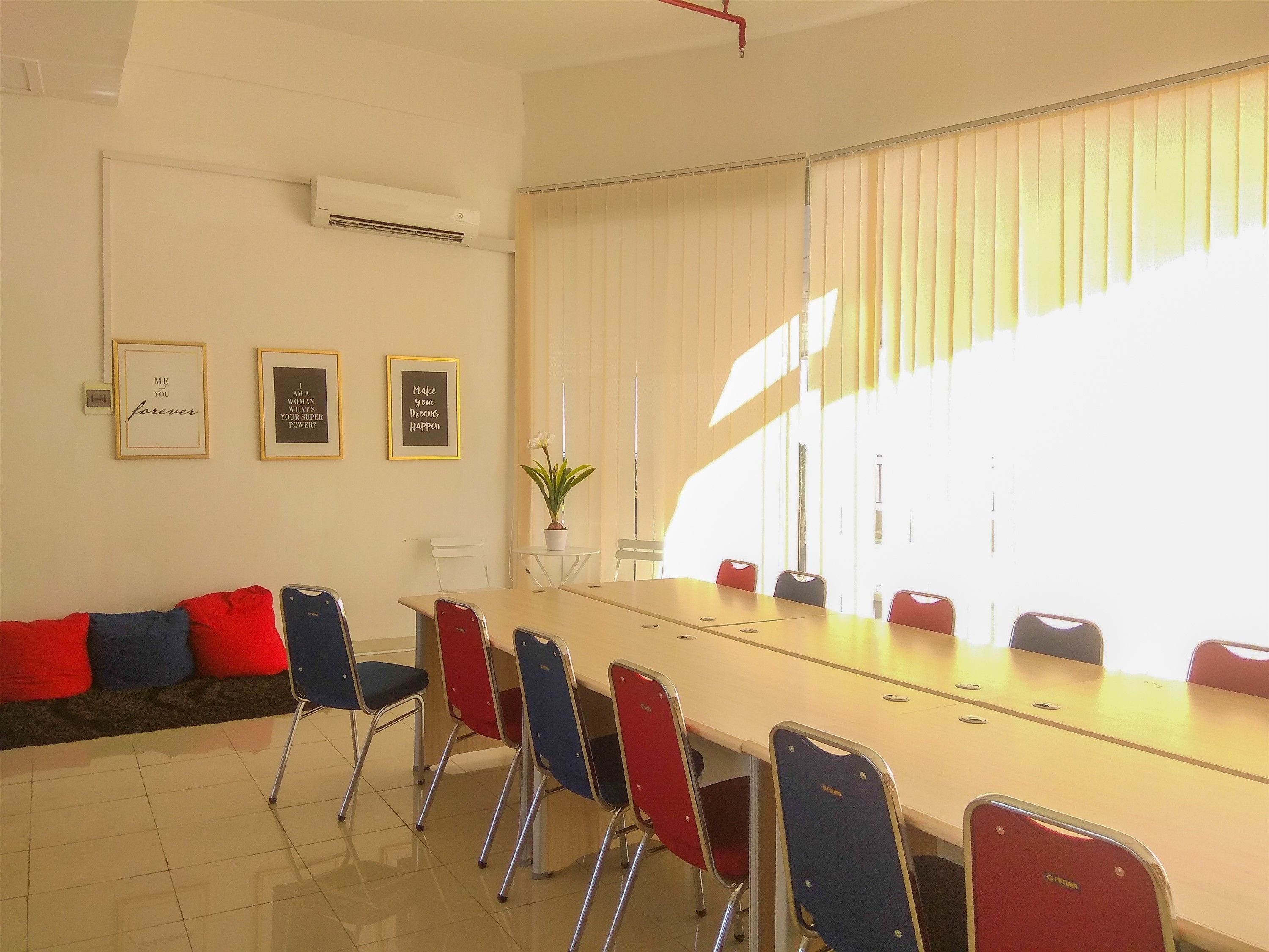 A conference room with a long table, red and blue chairs, and three motivational posters on the wall.