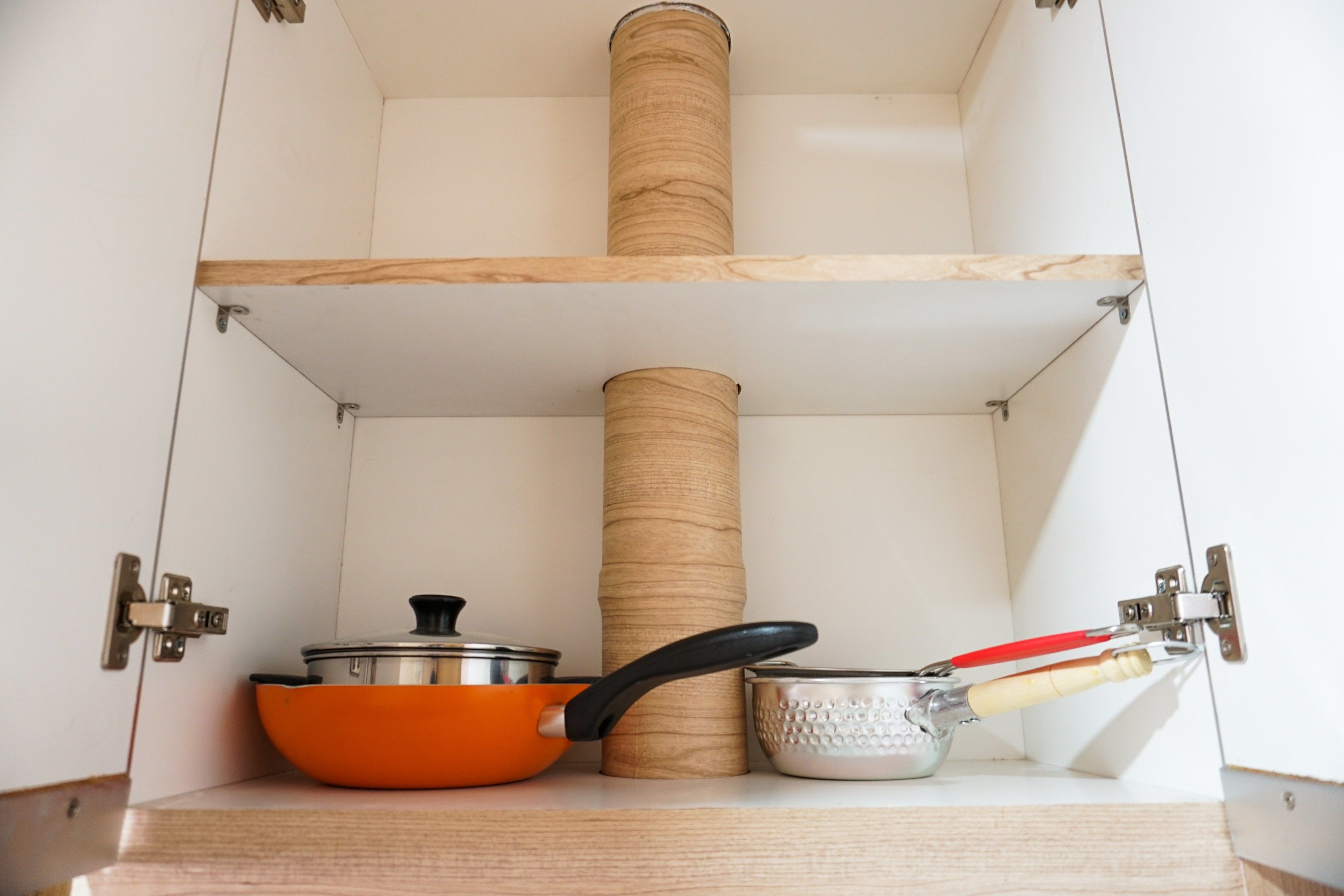 A kitchen cabinet with three shelves, each holding different kitchen utensils and cookware.
