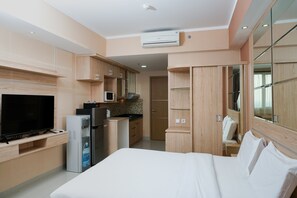 A modern hotel room with a flat-screen TV, a mini-fridge, a microwave, and a water dispenser. The room features wooden cabinetry and a large bed with white linens.