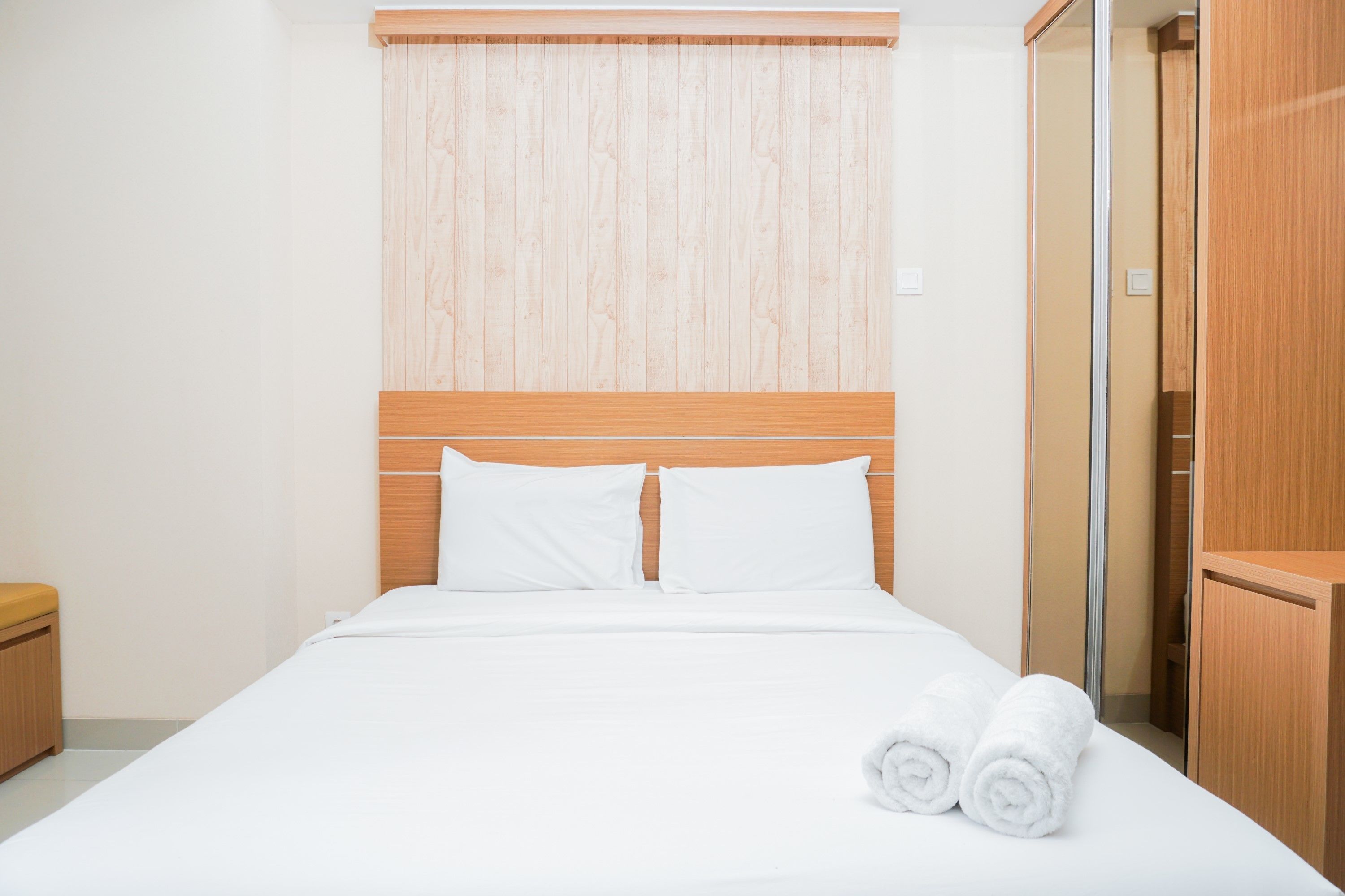 Una cama bien hecha con sábanas blancas y dos toallas enrolladas, un cabecero de madera y un armario de madera.