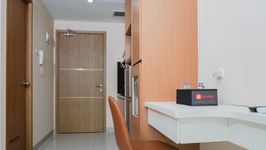 Una habitación de hotel con una puerta de madera, un escritorio blanco con un mini bar y una silla marrón.