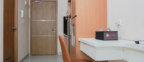A hotel room with a wooden door, a white desk with a minibar, and a brown chair.