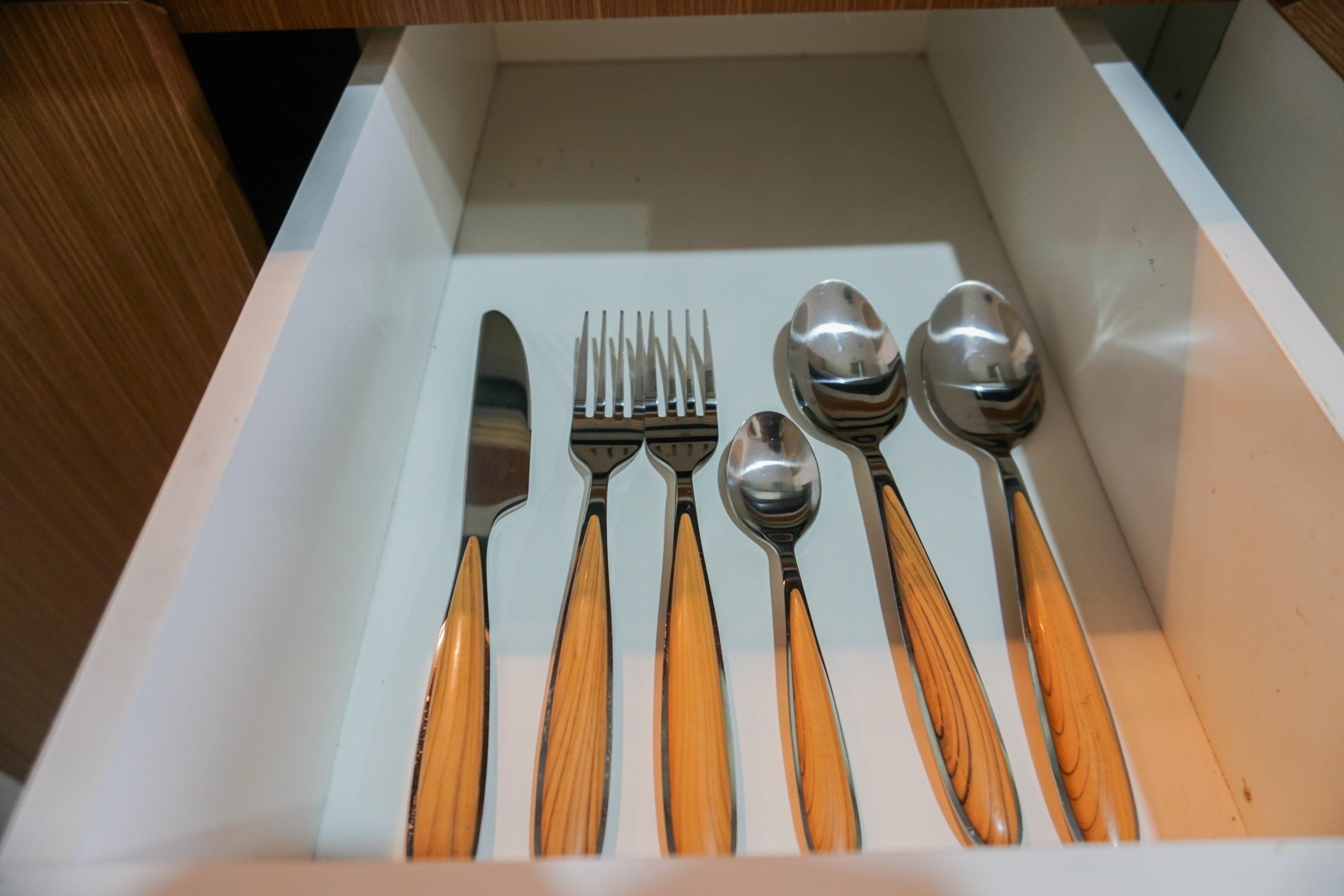 A drawer containing a knife, fork, spoon, and two spoons with wooden handles.