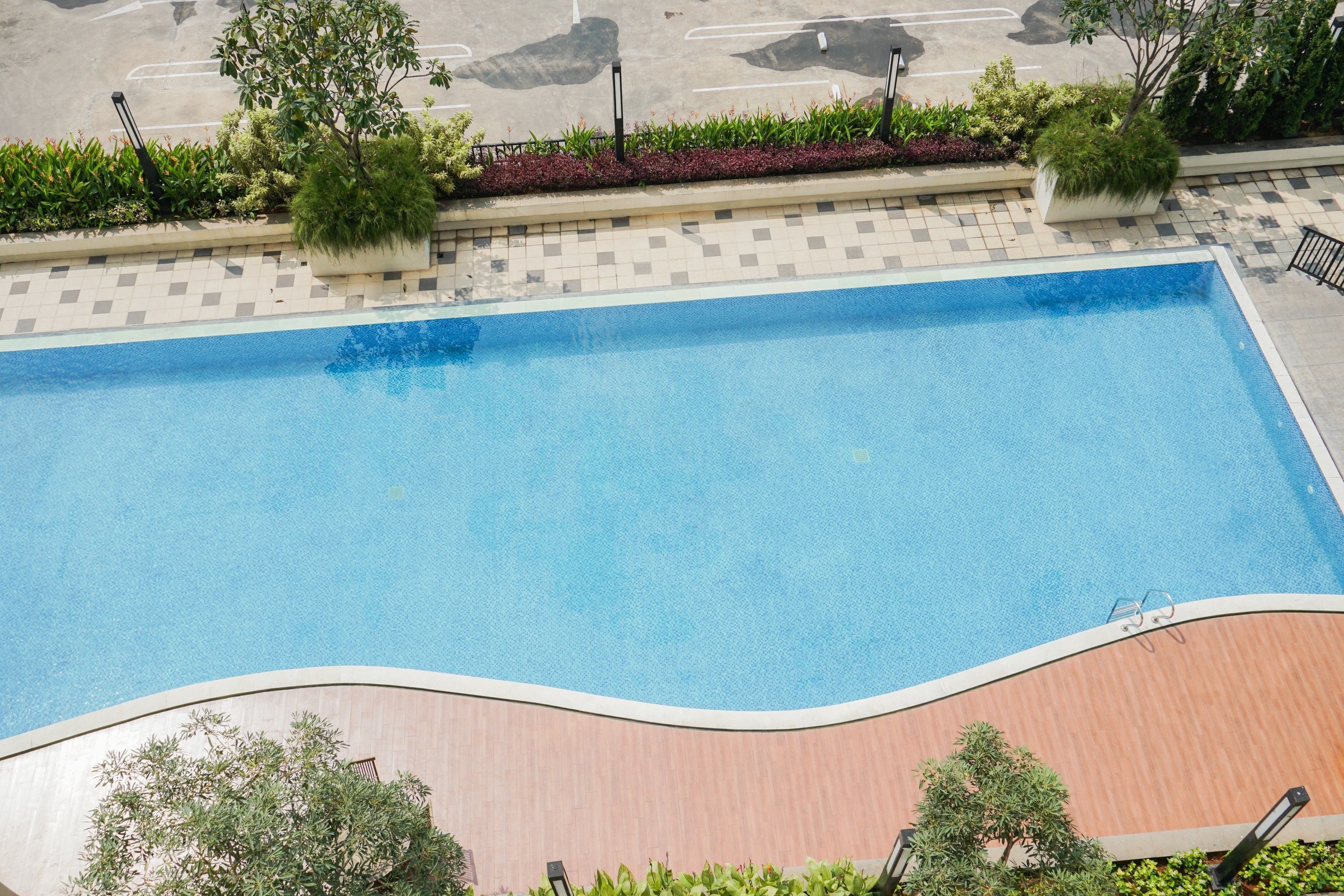 Une piscine rectangulaire entourée d’une terrasse en bois, bordée d’un chemin pavé et de verdure.
