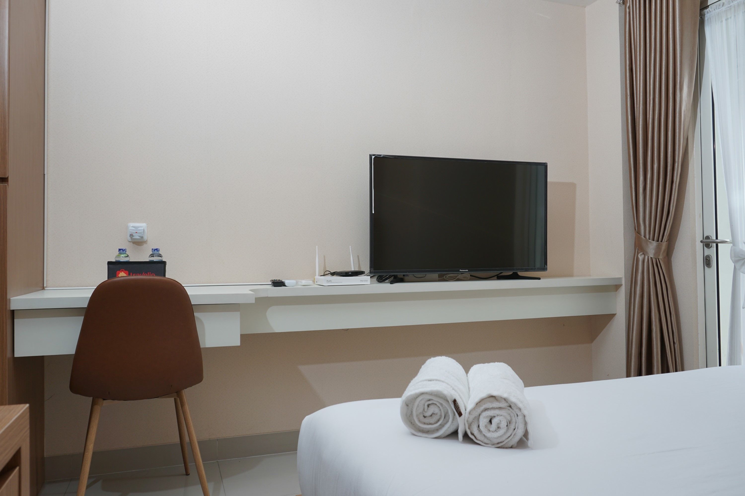 A hotel room with a bed, a desk with a television, a chair, and a bathroom with a curtain.