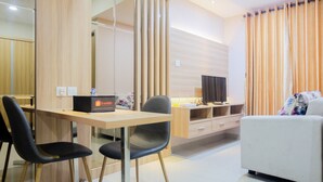 A modern living room with a sofa, a dining table with two chairs, a TV, and a cabinet. - Best Modern 1BR The Oasis Apartment (Cikarang)