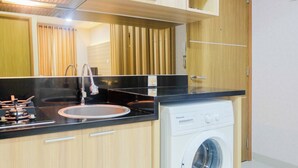 A modern kitchen with a built-in washing machine, a sink, and wooden cabinets. - Best Modern 1BR The Oasis Apartment (Cikarang)