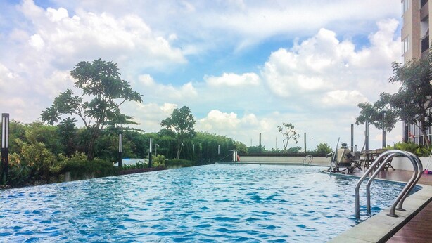 An outdoor swimming pool with a clear sky and surrounding greenery. - Best Modern 1BR The Oasis Apartment (Cikarang)