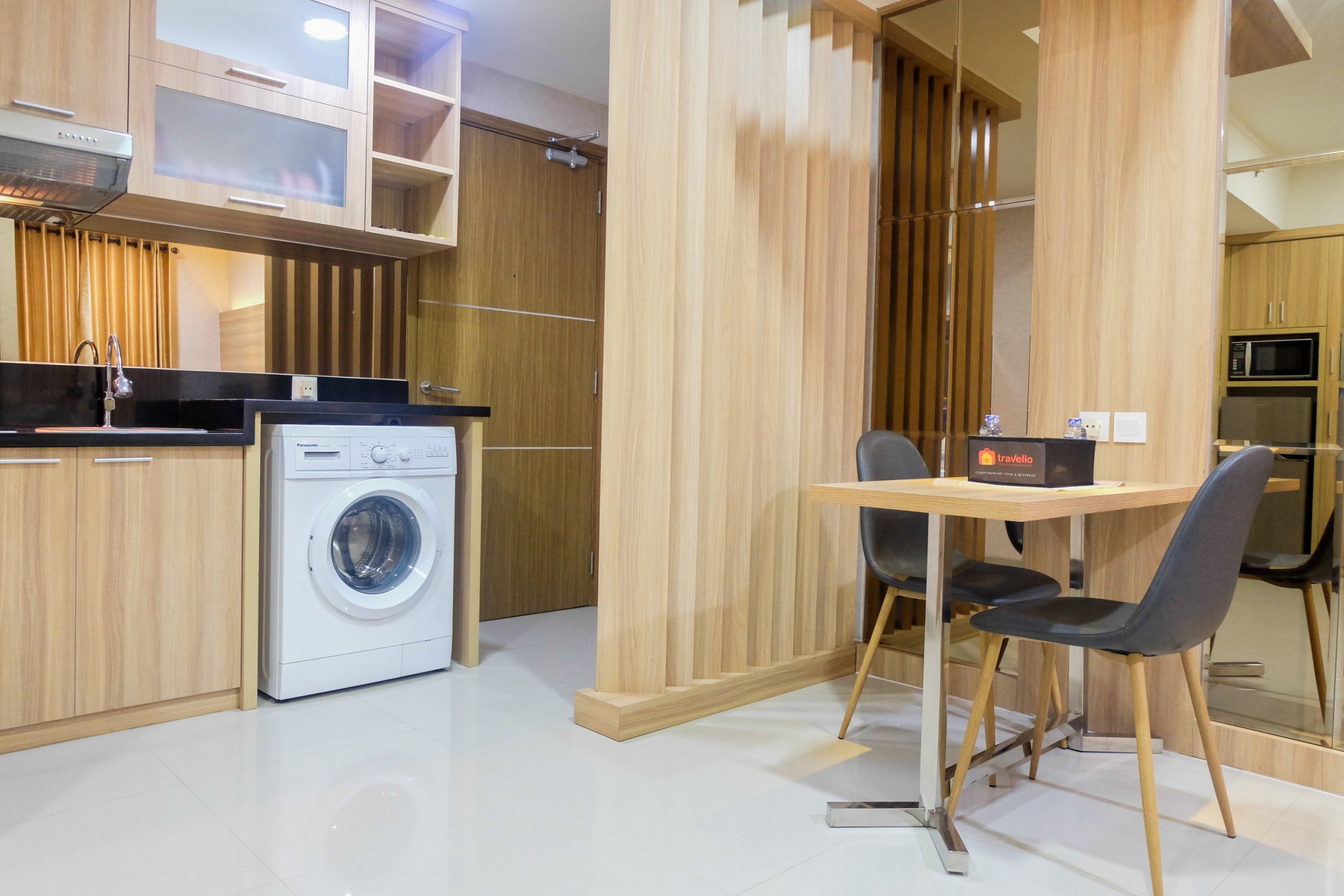 A compact kitchen with wooden cabinetry, a washing machine, a microwave, and a dining area with a table and chairs.