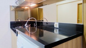 A modern kitchen with a black countertop, stainless steel faucet, and a range hood. - Best Modern 1BR The Oasis Apartment (Cikarang)