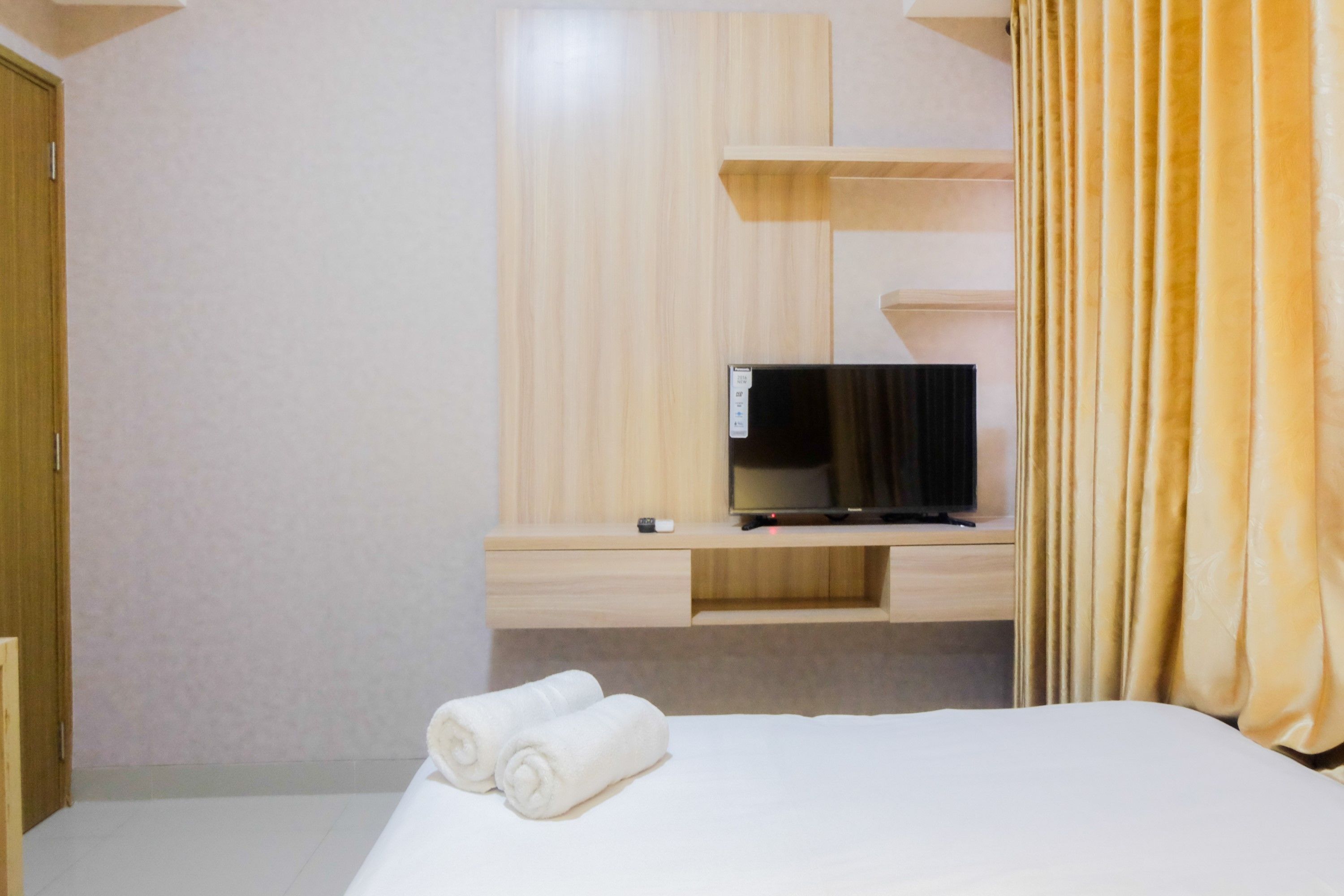 Una habitación de hotel con una cama, un televisor sobre un estante de madera y un par de toallas enrolladas sobre la cama.
