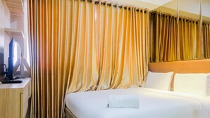 A hotel room with a large bed, a desk with a computer, and curtains. - Best Modern 1BR The Oasis Apartment (Cikarang)
