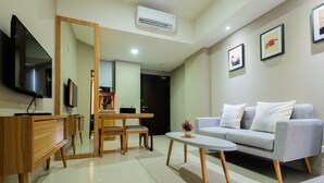 A modern living room with a grey sofa, a coffee table, a TV, and a dining area with a wooden table and chairs. - Best Location 1BR Mustika Golf Apartment (Cikarang)