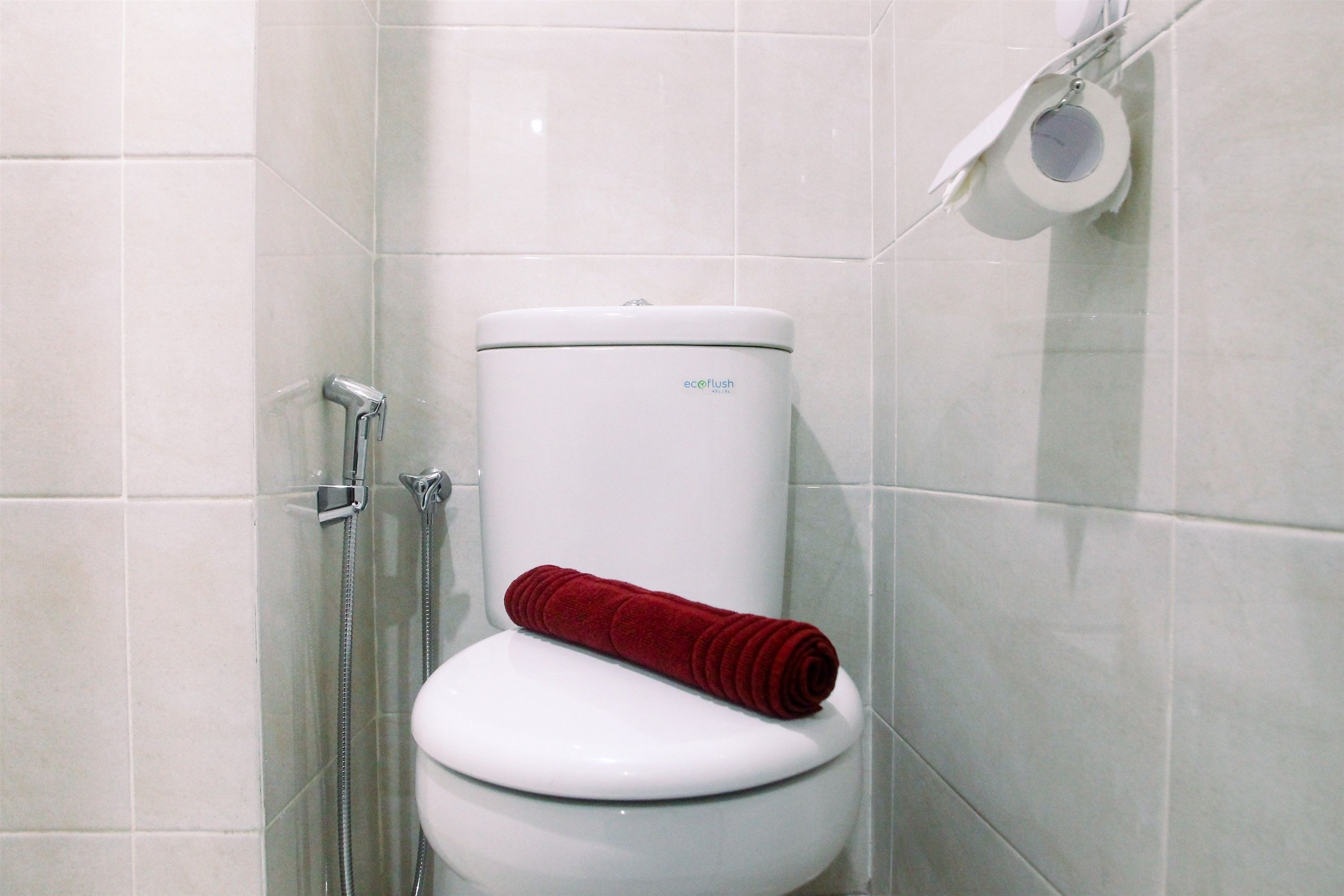 Des toilettes blanches avec une serviette rouge posée sur la lunette, une pomme de douche et un porte-rouleau de papier toilette fixé au mur.