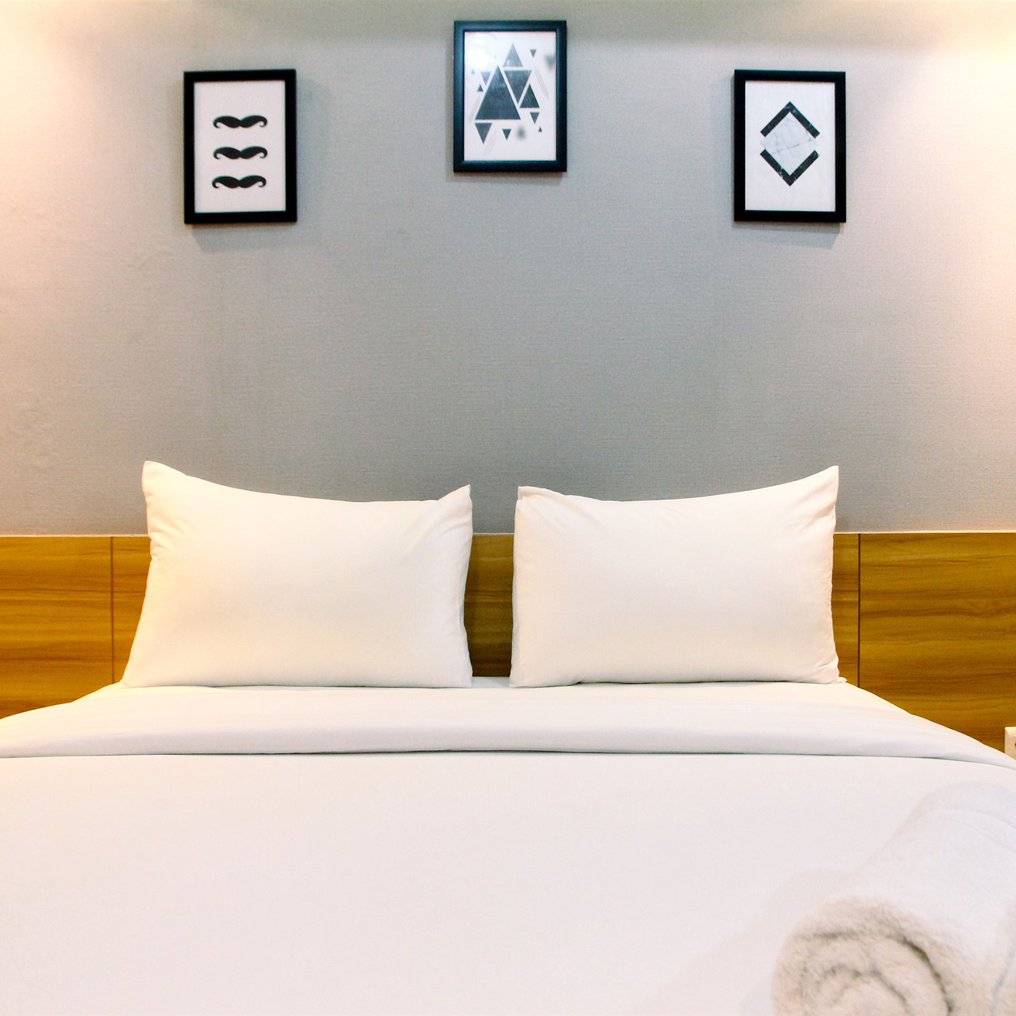 Una cama bien hecha con sábanas blancas y dos almohadas, un cabecero de madera y tres cuadros enmarcados en la pared de arriba.