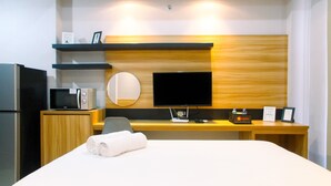 A hotel room with a bed, a desk with a computer, a TV, a microwave, and a refrigerator. - Modern and Comfy Studio @ Mustika Golf Apartment (Cikarang)