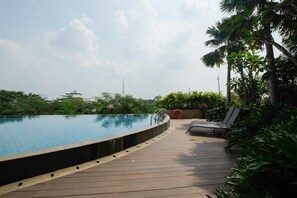 A wooden deck with a swimming pool, lounge chairs, and surrounding greenery. - Elegant Studio Mustika Golf Residence Apartment (Cikarang)