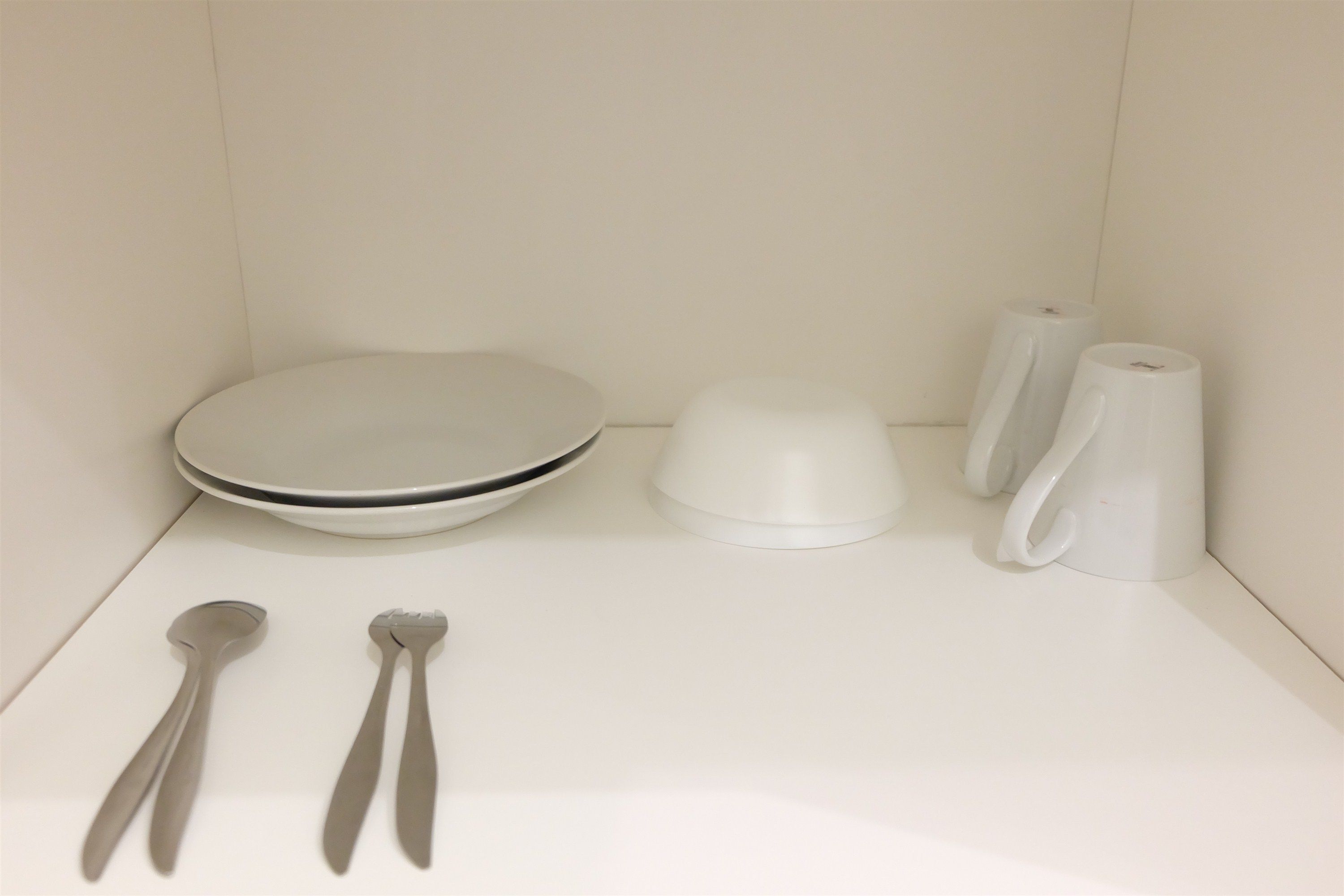 A white bathroom with a toilet, a sink, a mirror, and two metal spoons.